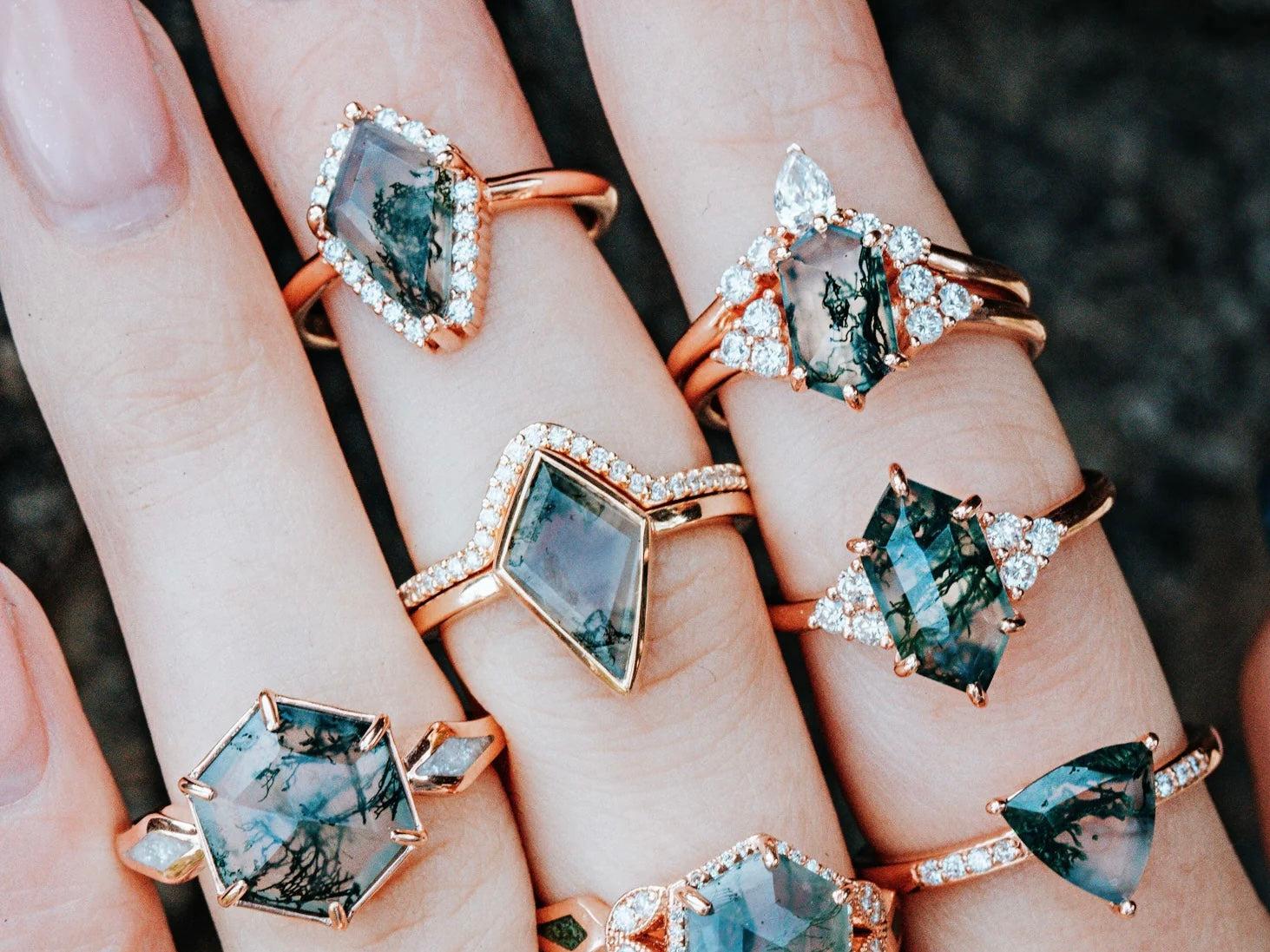 A person wears a variety of Moss Agate Engagement Rings on his hand.