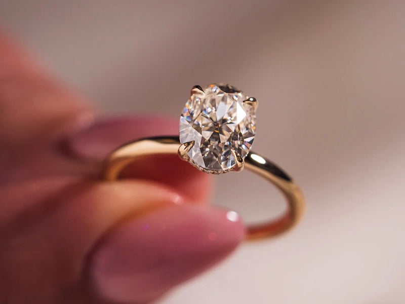 A close-up shot of a person's hand delicately holding up a gold engagement ring.