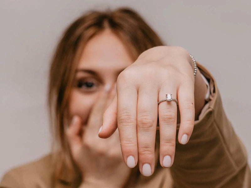 A woman, her face blurred with joy, extends her left hand to showcase a sparkling diamond engagement ring